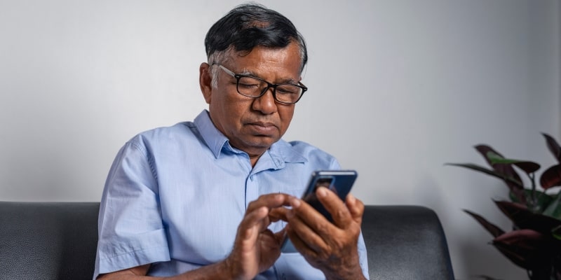 Um homem idoso mexendo no celular, lendo mensagens que recebe de um novo golpe contra idosos.