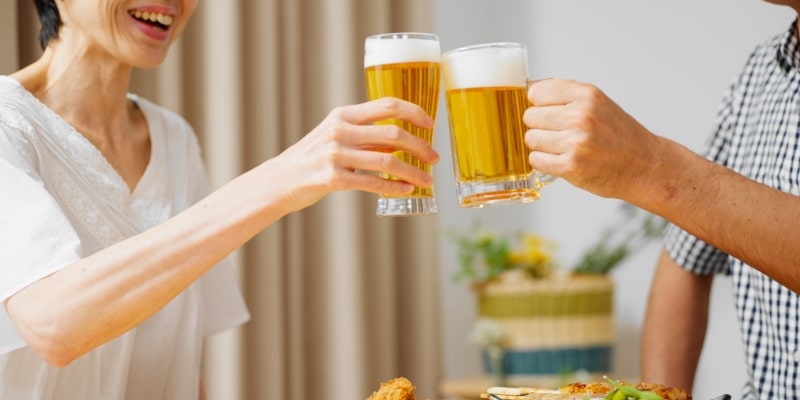 Um casal de pessoas idosas brindando com copos de cerveja. Imagem para ilustrar a matéria sobre relação entre álcool e envelhecimento.