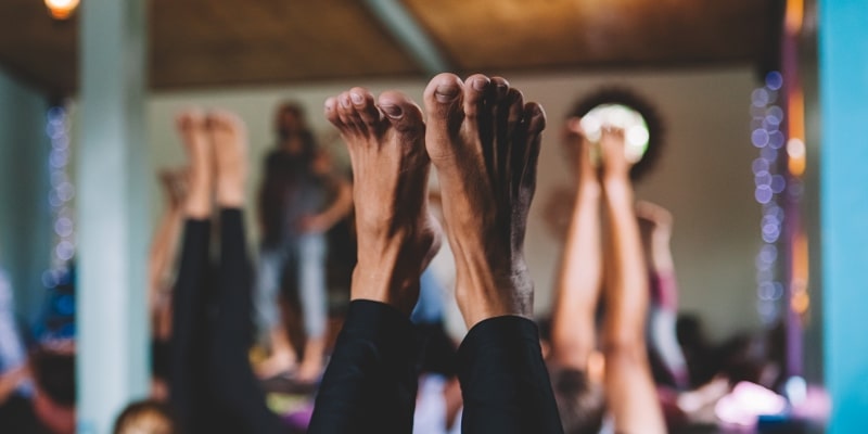 Pessoas suando praticando hot yoga. Foco nos pés elevados.