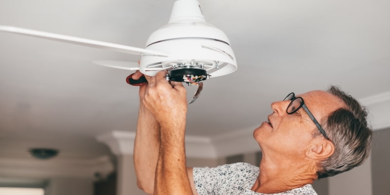 Um senhor eletricista, consertando um ventilador de teto. Imagem para ilustrar a matéria sobre trabalho depois dos 60 anos.