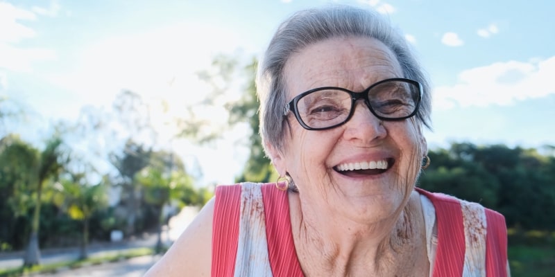 Um senhora sorrindo alegremente. Imagem para ilustrar a matéria sobre hábitos que promovem a felicidade.