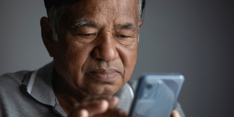 Um senhor mexendo no celular, enquanto percebe que está caindo em um novo golpe contra aposentados.