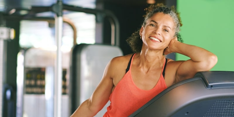 Uma mulher idosa, sorrindo, após fazer exercício na esteira. Imagem para ilustrar a matéria sobre treinamento físico para idosos.