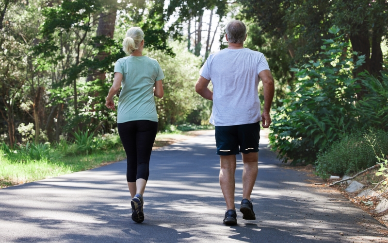 Um casal de idosos caminhando no parque, mostrando que andar rápido tem diversos benefícios.