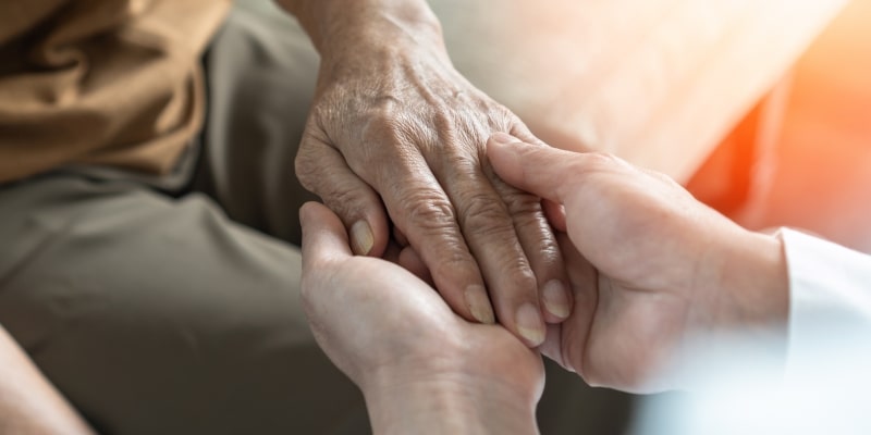 Uma pessoa de mãos jovens segurando a mão de uma pessoa idosa para aliviar o desgaste mental de idosos no fim do ano.