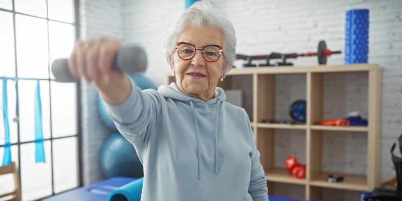 Uma mulher idosa praticando musculação. Imagem para ilustrar a matéria sobre hábitos que desaceleram o processo de envelhecimento.