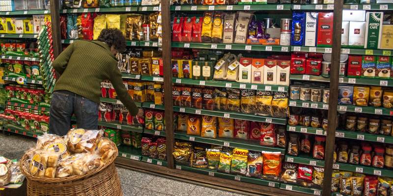 Um senhora pegando café, um dos alimentos com tarifa zero, em uma prateleira de mercado.