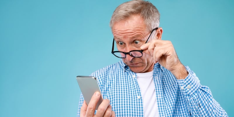 Um homem idoso olhando o celular e chocado ao ver a notícia falsa dizendo que aposentadoria será de 78 anos.