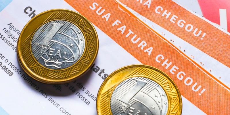 Moedas de um real sobre uma conta de luz escrito 