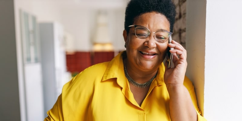 Uma mulher associada ao Instituto de Longevidade falando ao telefone com o escritório, ao usar o benefício de Amparo Jurídico. Ela é negra e sorri.
