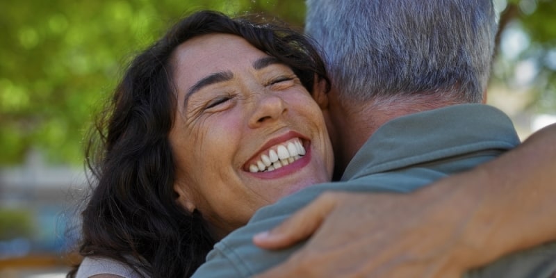 Uma mulher sorrindo ao abraçar o seu amigo. Imagem para ilustrar a matéria sobre conexões sociais.
