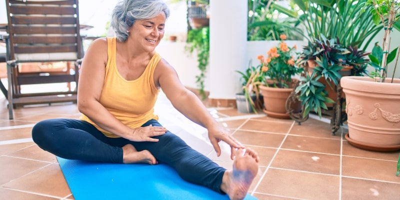 Uma mulher, com cerca de 50 anos, alongando em uma varanda. Imagem para ilustrar a matéria sobre a medicina da longevidade.