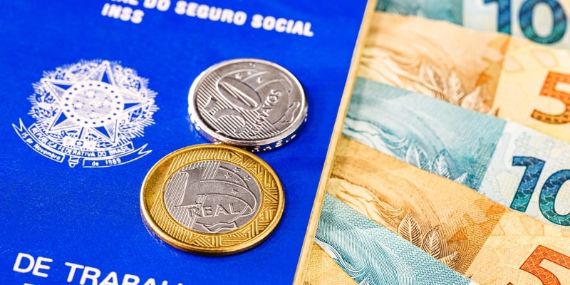 Carteira de trabalho brasileira antiga, com moedas e notas de real. Imagem para ilustrar a matéria sobre a resposta sobre os descontos indevidos do INSS.