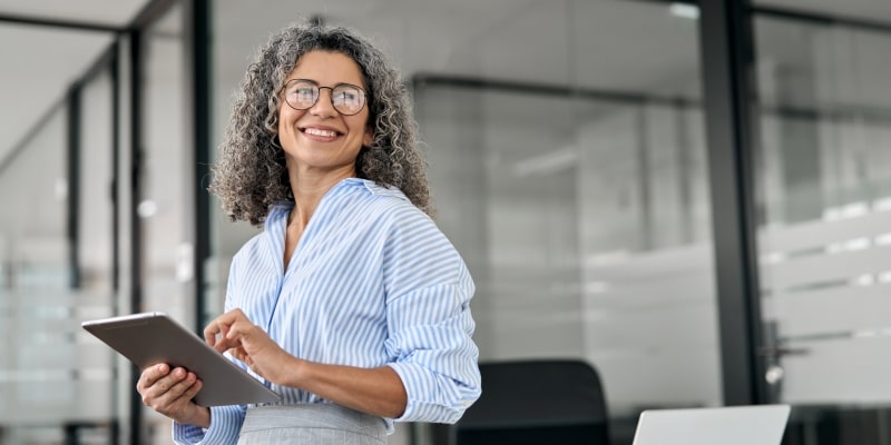Uma mulher madura sorrindo em um ambiente de trabalho. Imagem para ilustrar a matéria sobe a revolução dos 50+