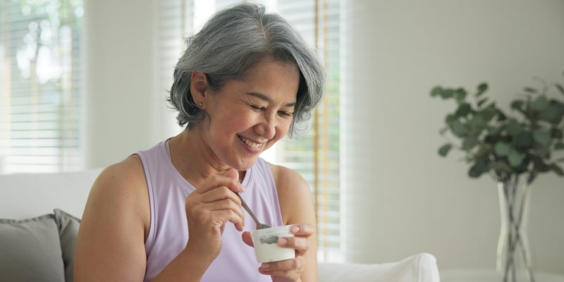 Uma mulher comendo iogurte, alimento que é considerado bom para a conexão entre intestino e cérebro.