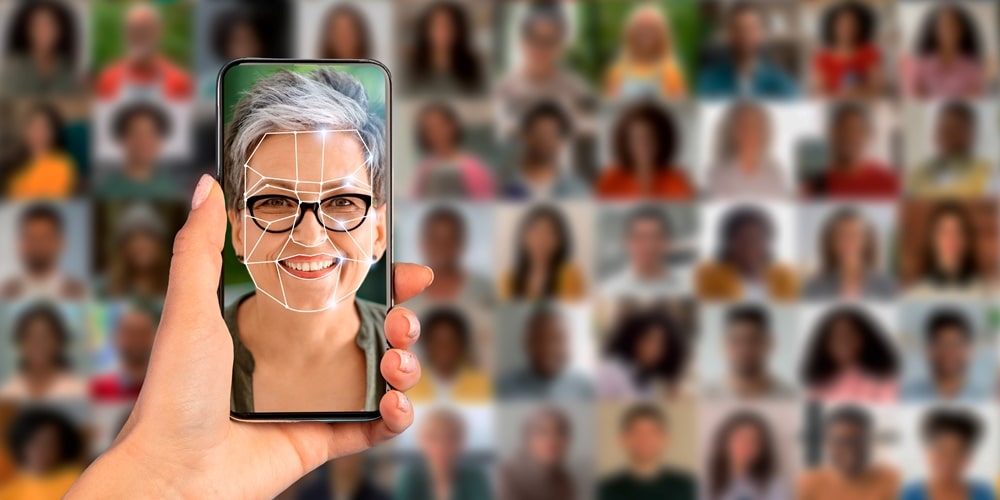 Tecnologia de reconhecimento facial por celular para identificar indivíduos. Tela do celular, o rosto de uma idosa sorrindo. Ao fundo, rostos desfocados. Imagem para ilustrar a matéria sobre o golpe do reconhecimento facial.