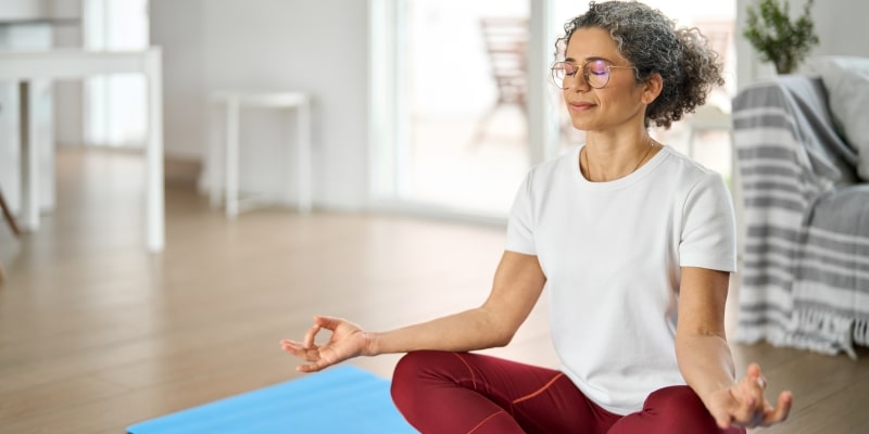 Uma mulher madura meditando em sua sala, em busca de mais qualidade de vida na menopausa.