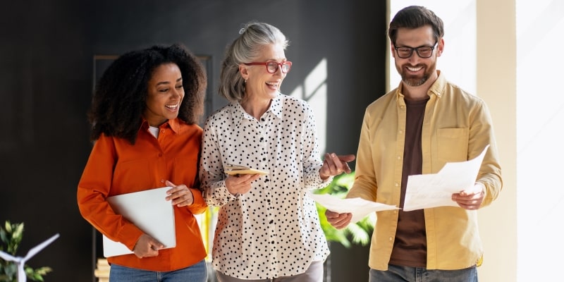Dois talentos jovens e uma profissional senior rindo no escritório.