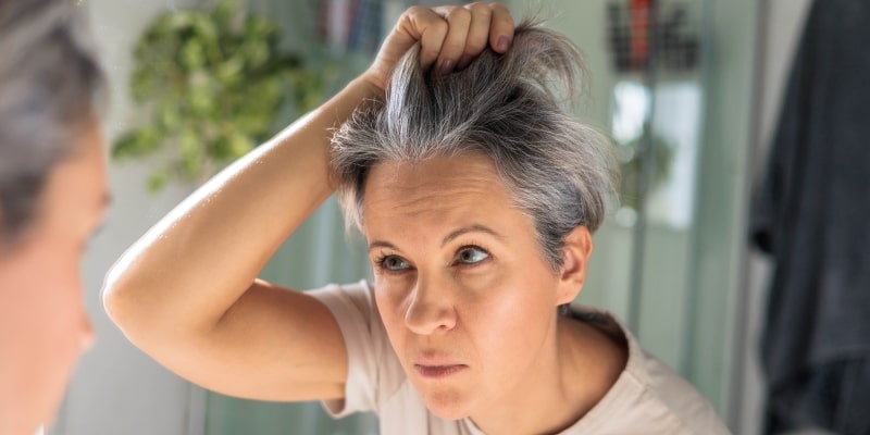 Um mulher olhando seu cabelo branco no espelho.