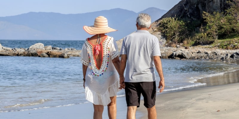 Um casal de idosos caminhando na beira da praia. Imagem para ilustrar a matéria sobre morar perto do mar aumenta a expectativa de vida.