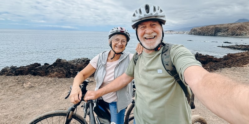 Idosos ativos se divertindo tirando uma foto de selfie com câmera ao andar de bicicleta. Imagem para ilustrar a matéria sobre mudar hábitos de saúde.