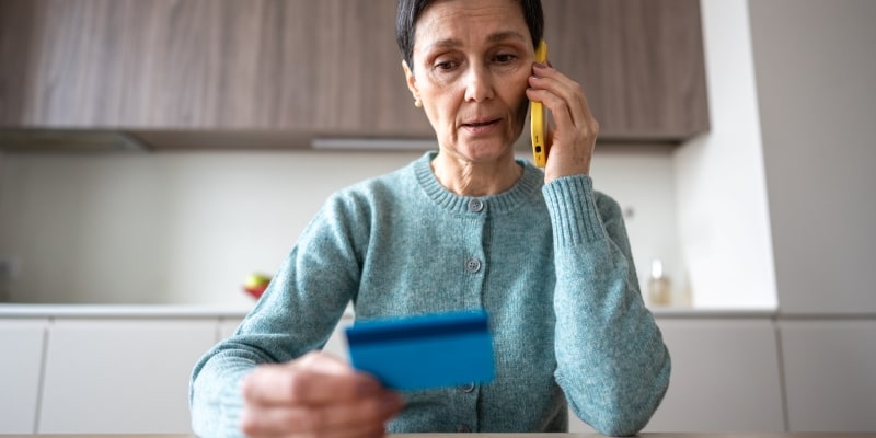 Uma senhora falando ao celular e olhar com preocupação com o cartão de crédito. Imagem para ilustrar a matéria sobre os sinais de demência financeira.