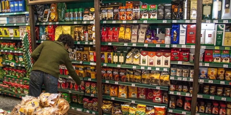 Um mulher pegando um pacote de café em uma prateleira de mercado na seção de cafés. Imagem para ilustrar a matéria sobre aumento no preço do café.