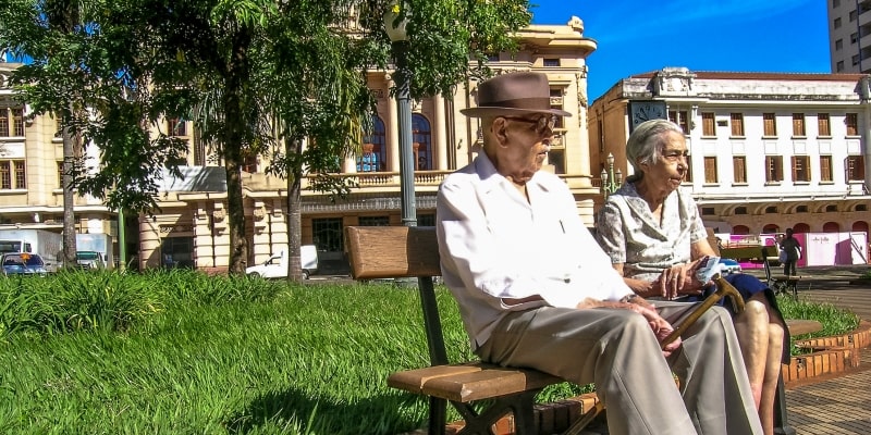 Um casal de idosos sentado em uma praça. Imagem para ilustrar a matéria sobe loteraria do envelhecimento.