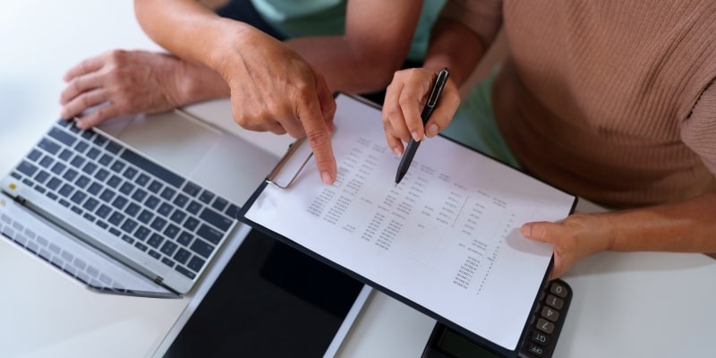 Um casal de idosos fazendo o seu planejamento financeiro aos 60 anos com calculadora, anotações, um tablet e um notebook.