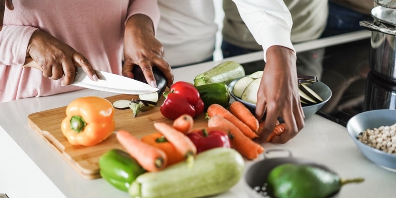 Uma família cortando legumes na cozinha para preparar uma comida nutritiva. Imagem para ilustrar a matéria sobre alimentos que aumentam risco de demência..