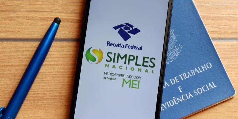 Um celular com um aplicativo do simpels nacional sobre uma carteira de trabalho, ilustrando a matéria sobre diferença entre MEI e autônomo.