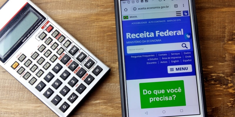 Um calculadora sobre uma mesa. Ao lado, um celular com o site da Receita Federal aberto. Imagem para ilustrar a matéria sobre a isenção de IR até 5 mil reais.