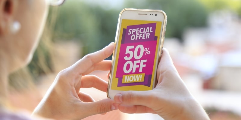 Uma mulher segurando um telefone que tem a mensagem "Oferta especial - 50% off agora" em inglês, ilustrando a matéria sobre busca por promoções.