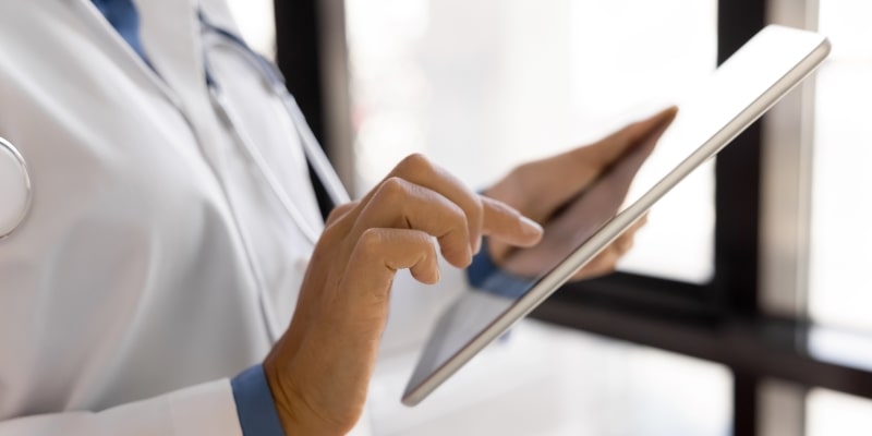Uma profissional de saúde, usando jaleco, mexendo em um tablet. Imagem para ilustrar a matéria sobre cancelamento de plano de saúde.