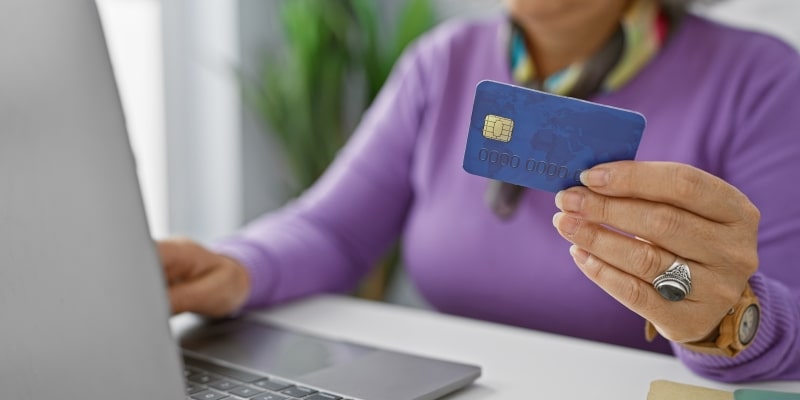 Uma mulher segurando um cartão de crédito enquanto mexe em um computador. Imagem para ilustrar a matéria sobre cartão salvo.