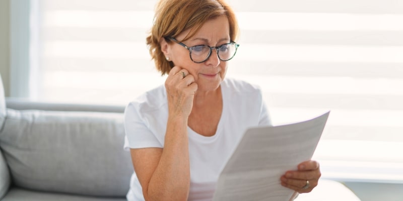 Uma mulher idosa sentada no sofá e olhando contas, pensando em como economizar na aposentadoria.