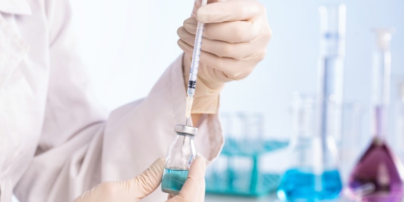 Em um ambiente controlado, mãos com luvas seguram frasco de vacina. Imagem para ilustrar a matéria sobre coração e vacinas.