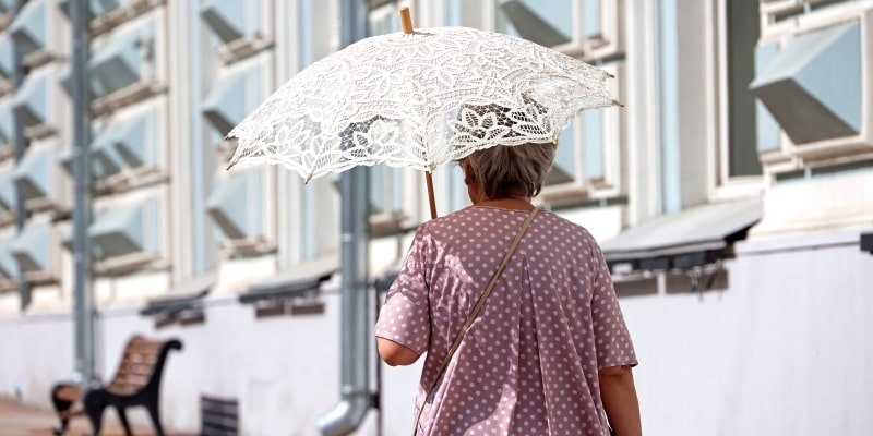 Uma mulher idosa andando na rua e se protegendo sol com um guarda chuva. Imagem para ilustrar a matéria sobre os desafios do aumento na expectativa de vida.