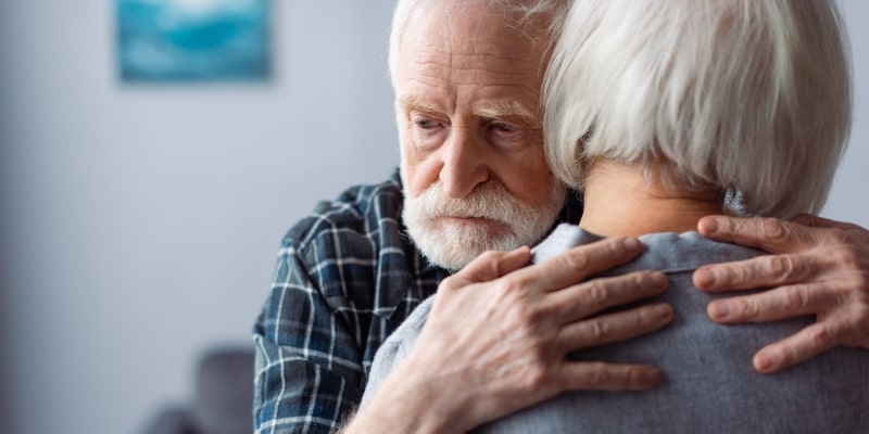 Um homem idoso abraçando uma mulher idosa com o olhar triste. Imagem para ilustrar a matéria sobre a diferença entre cérebro masculino e feminino.