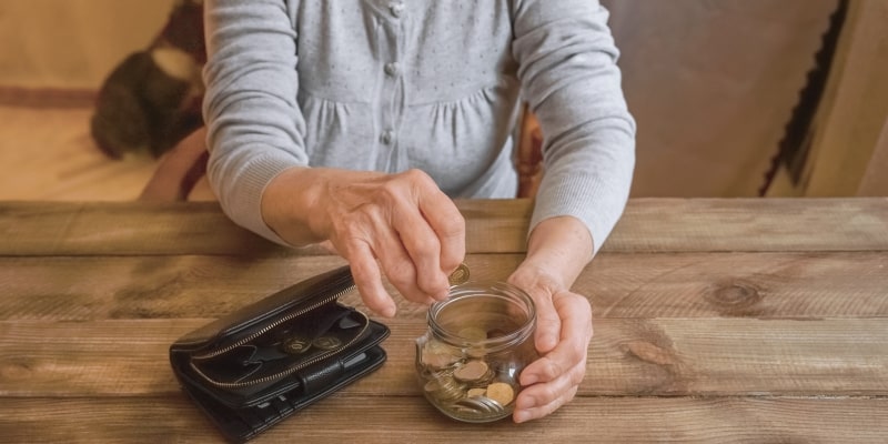 Mãos de uma senhora colocando moedas em um pote de vidro, ilustrando a matéria sobre estratégias para a aposentadoria.