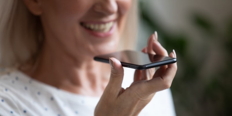 Uma mulher idosa falando com inteligência articificial no celular enquanto sorri. Imagem para ilustrar a matéria sobe IA para o público 50+.