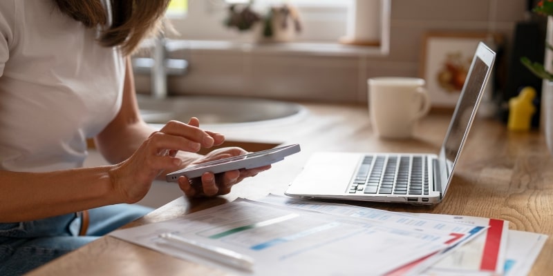 Uma mulher, mexendo no celular e no notebook, com papéis de planejamento financeiro, tentando entender melhor sobre os mitos sobre a Previdência Privada.