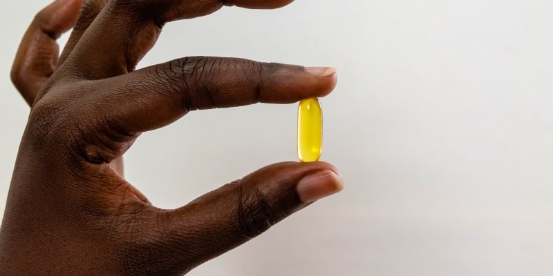 Uma mão de uma mulher de pele negra segurando uma cápsula de vitamina D.