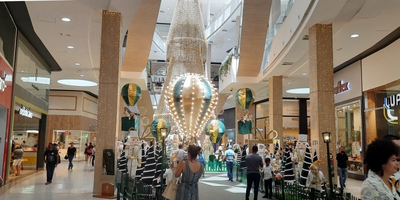 Um interior de um shopping, com pessoas circulando, e decoração de natal, ilustrando a matéria sobre escala de fim de ano.