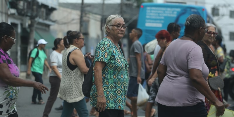 Um muher idosa atravessando a rua, junto com outras pessoas. Imagem para ilustrar a matéria sobre expectativa de vida saudável no Brasil.