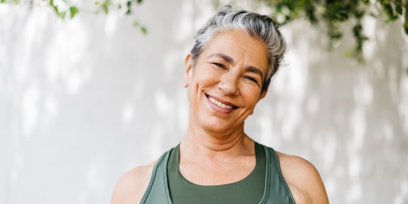 Uma mulher em torno de 40 ou 50 anos, com cabelos curtos e grisalhos sorrindo. Imagem  para ilustrar a matéria sobre hábitos para ter uma mente saudável.