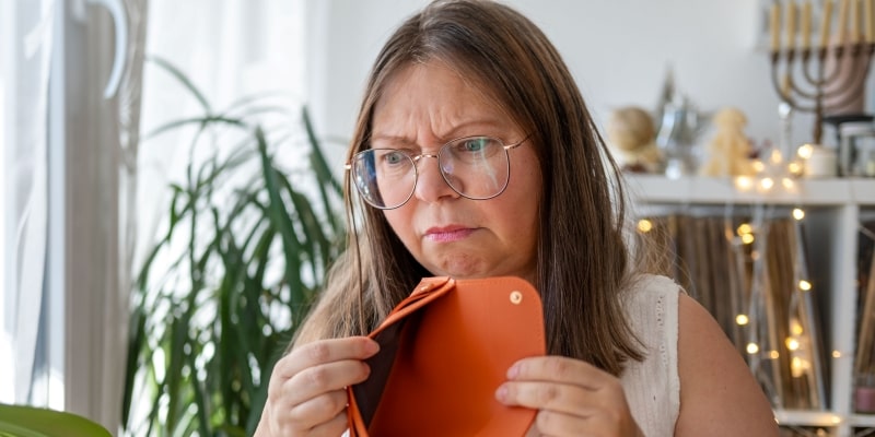 Mulher triste segurando carteira laranja vazia, sem dinheiro, ilustrando a matéria sobre insegurança financeira da Geração X.