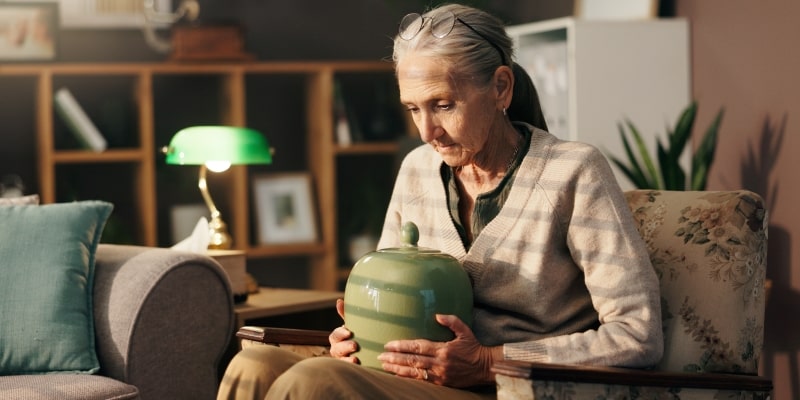 Uma mulher idosa solitária segurando uma urna no colo. Imagem representando solidão e medo de morrer sozinho.