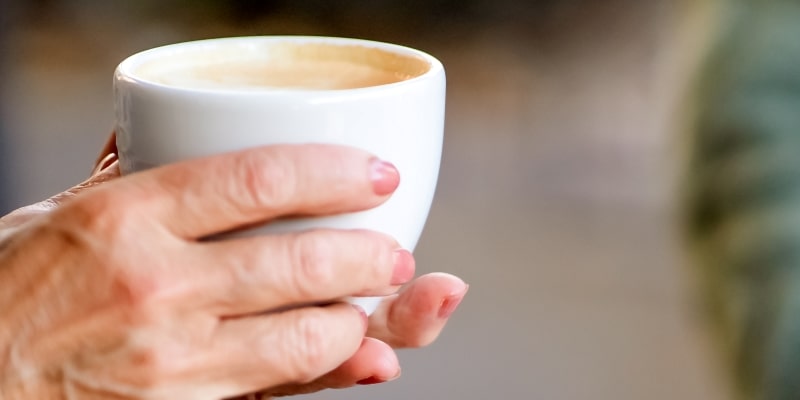 Mãos de uma mulher idosa segurando uma xícara de café, ilustrando a matéria sobre bebidas que aumentam a pressão arterial.