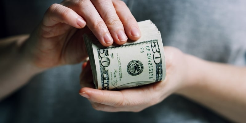 Uma mão feminina segurando um bloco de notas de dólar 2026.